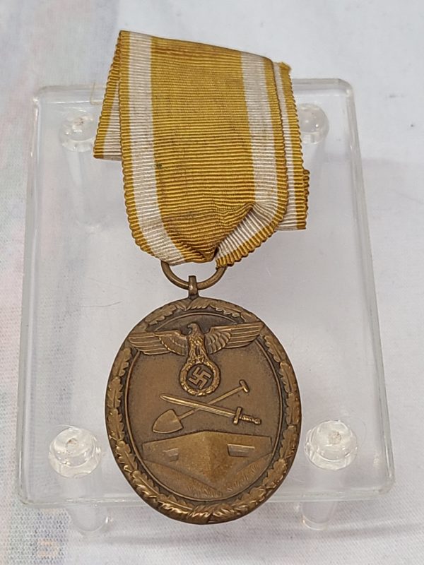 Antique German Medal with a yellow ribbon and a picture of an eagle holding the Nazi symbol with a shovel and sword crossed underneath and a building at the very bottom